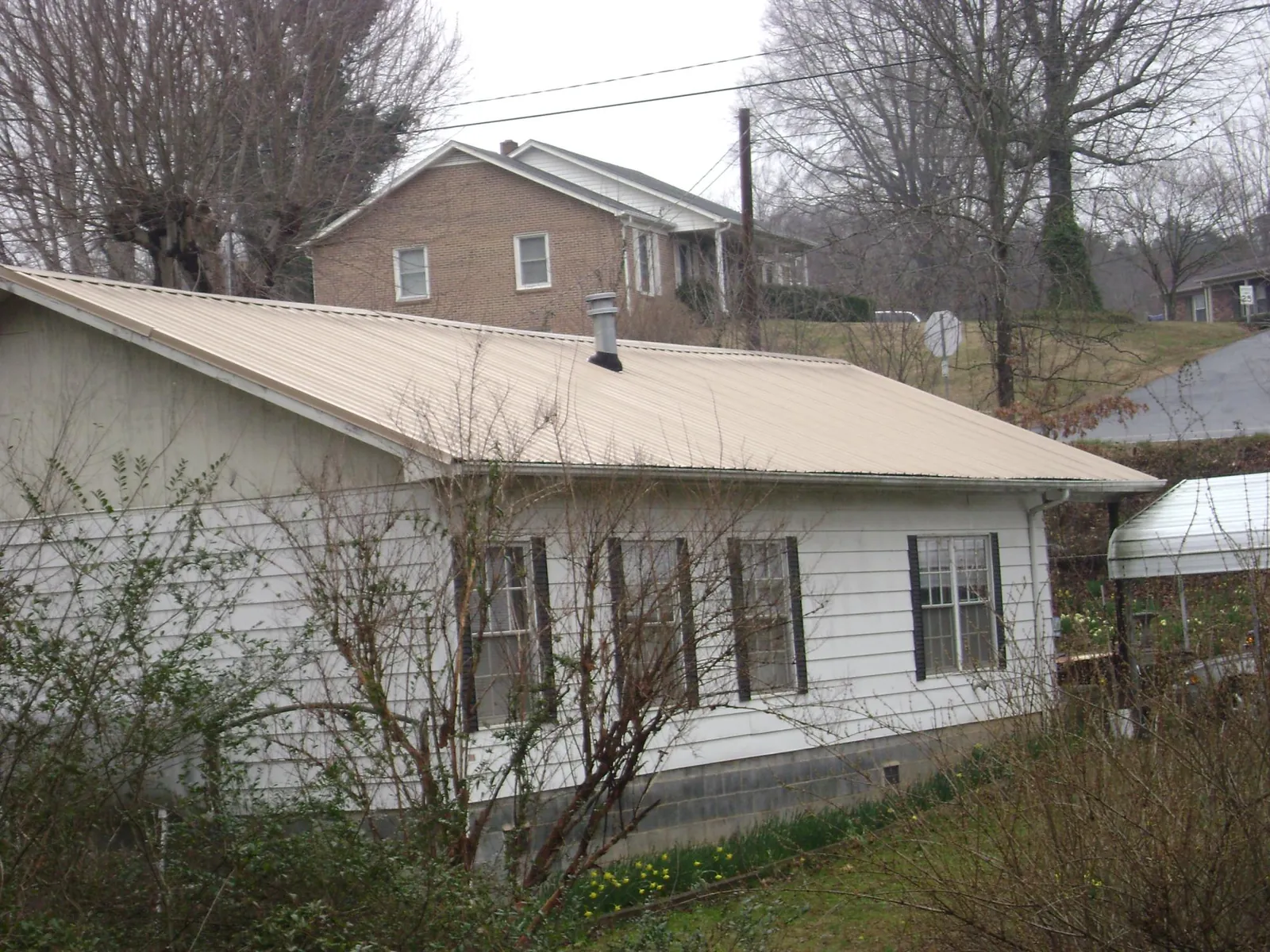 Tan metal roof on a white sided house set into a hillside — Commercial Roofing by Roofing Brothers in Madison